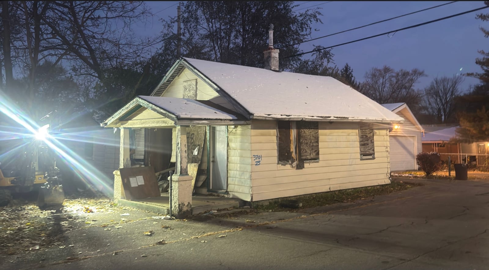 A fire-damaged single-story house with boarded windows at dusk