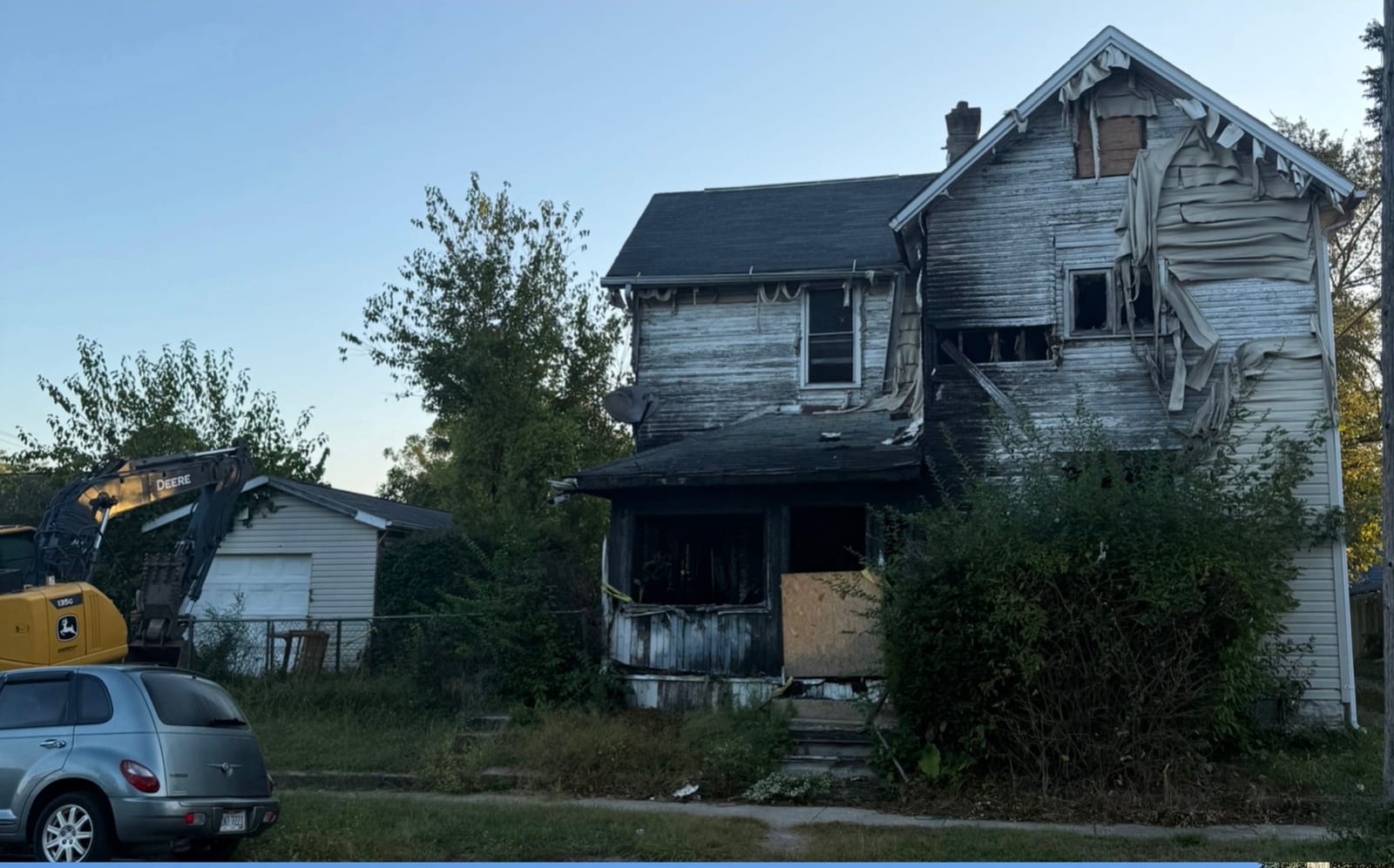 A derelict two-story house with broken windows and siding
