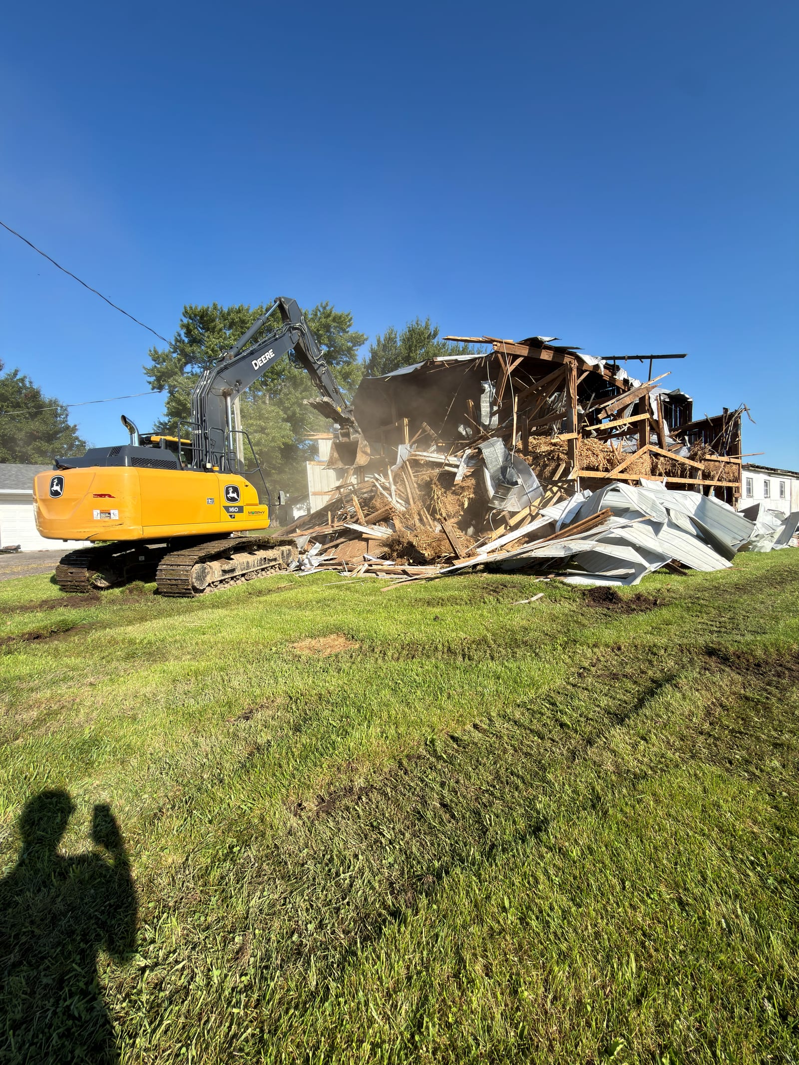 A tracked excavator tearing down a farm outbuilding on a clear day