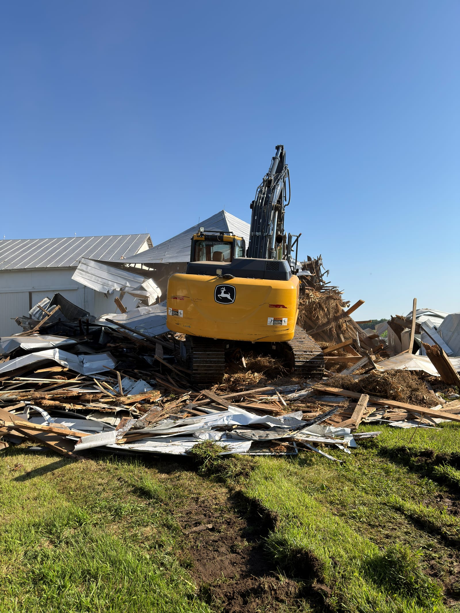 An excavator sorting torn metal roofing and timber from a demolished building into a debris pile