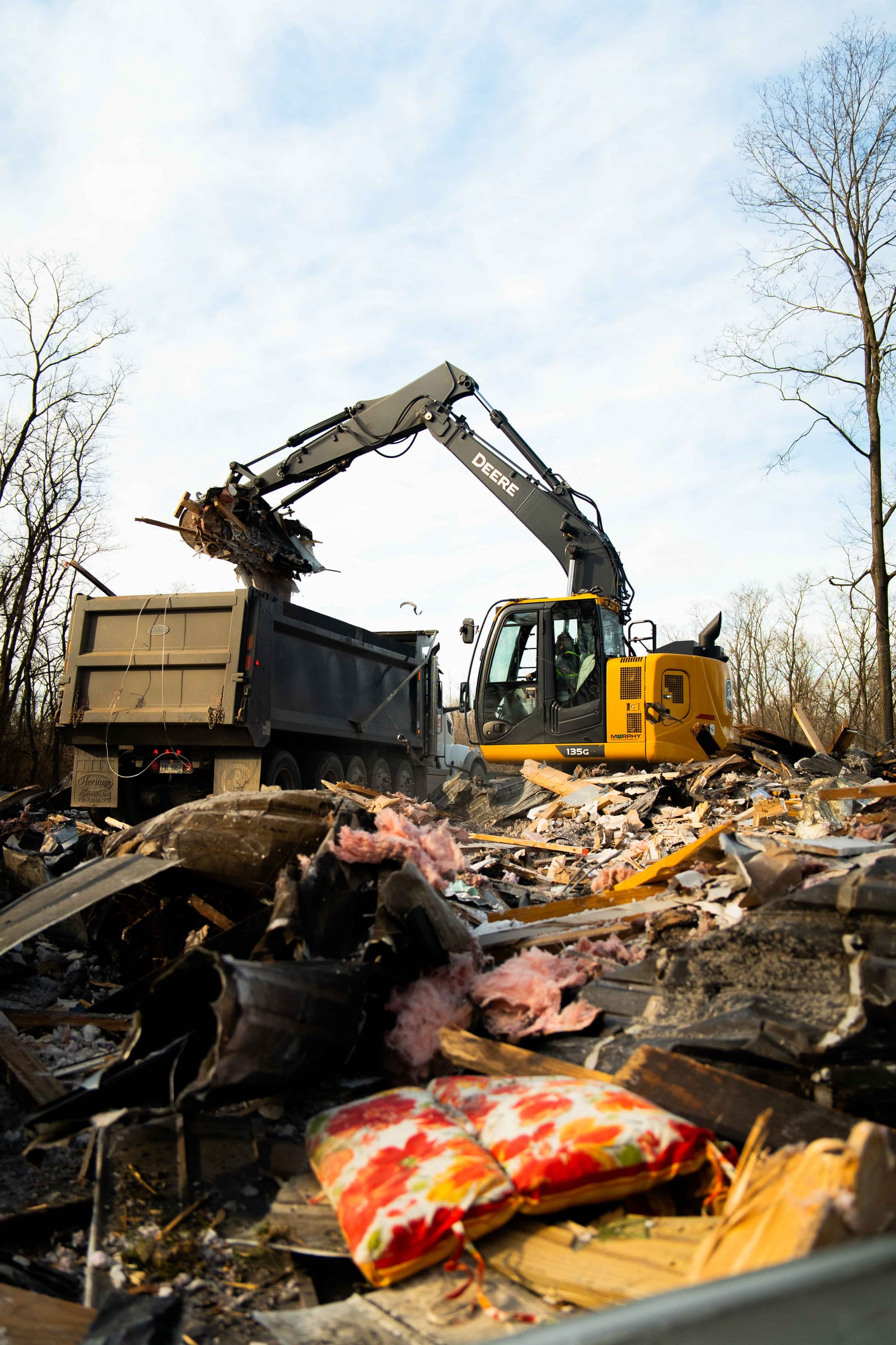 An excavator lifting scrap and timber into a dump truck during a property clear-out