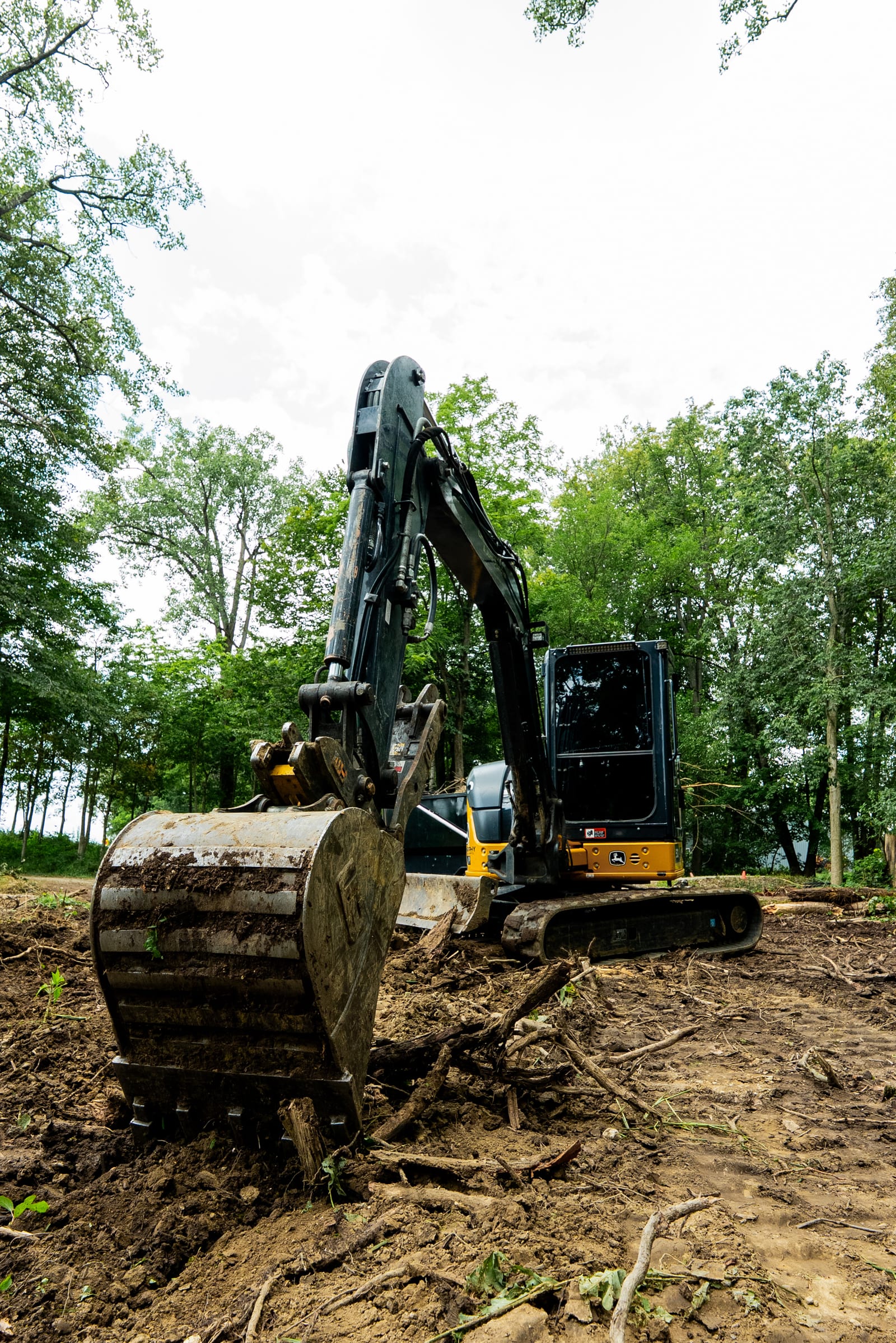 An excavator clearing ground along a tree line on a spring day